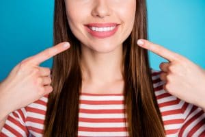 Cropped close up photo of positive girl point index finger her teeth, recommend whitening beaming veneers treatment wear red style stylish trendy shirt isolated blue color background